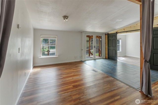 empty room with a barn door, hardwood / wood-style floors, baseboards, vaulted ceiling, and a textured ceiling