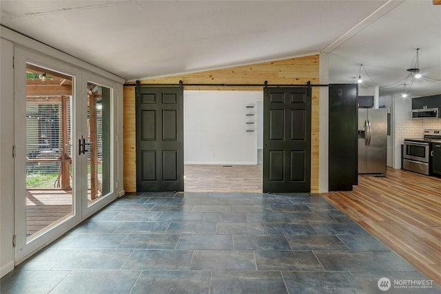 entrance foyer with a barn door, vaulted ceiling, wooden walls, and baseboards