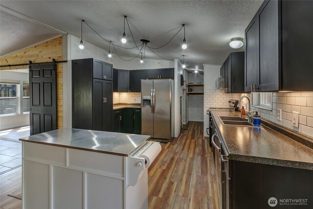 kitchen featuring appliances with stainless steel finishes, a barn door, a sink, dark countertops, and wood finished floors