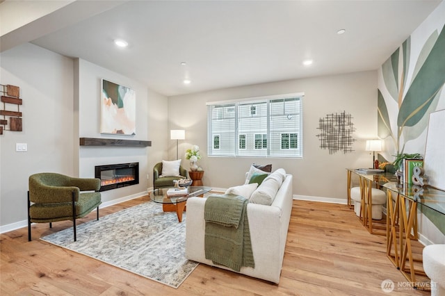 living area featuring a glass covered fireplace, light wood-style flooring, baseboards, and recessed lighting