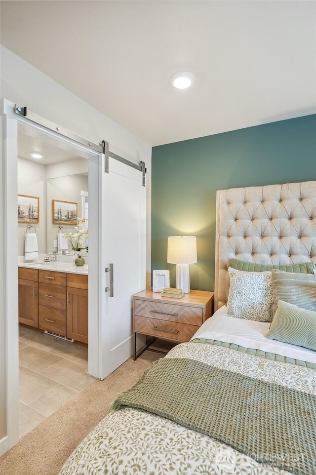 bedroom with a barn door, light colored carpet, ensuite bathroom, and light tile patterned floors
