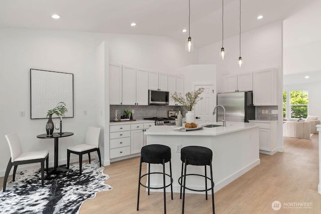 kitchen featuring stainless steel appliances, a sink, light wood-style flooring, backsplash, and a breakfast bar