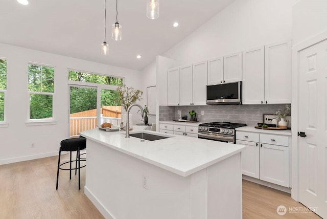 kitchen with a sink, appliances with stainless steel finishes, tasteful backsplash, light wood-style floors, and high vaulted ceiling