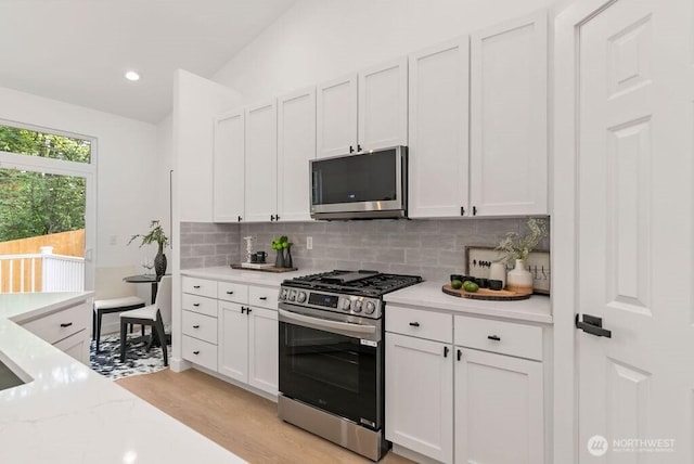 kitchen featuring stainless steel appliances, light wood-style floors, white cabinetry, backsplash, and lofted ceiling