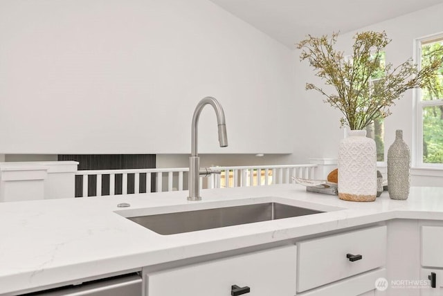 kitchen view of a sink, white cabinetry, light stone countertops, and dishwasher