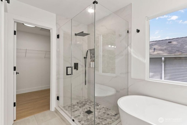 full bath with a freestanding bath, a marble finish shower, a spacious closet, and baseboards