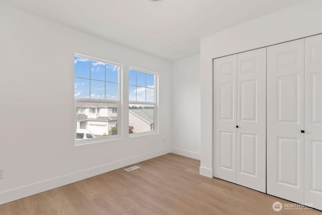 unfurnished bedroom featuring baseboards, light wood finished floors, and a closet