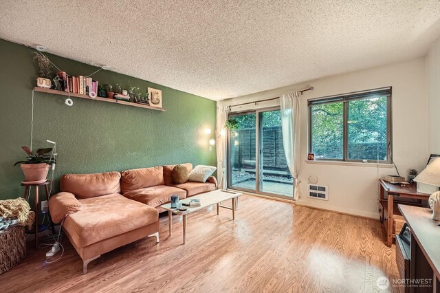 living area with a textured ceiling, wood finished floors, heating unit, and a textured wall