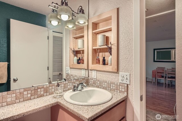 bathroom with tasteful backsplash, vanity, wood finished floors, and a textured wall