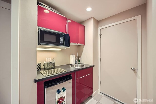 kitchen featuring black microwave, red cabinetry, refrigerator, dark countertops, and a sink
