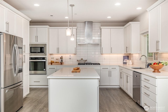 kitchen featuring stainless steel appliances, wall chimney range hood, a sink, light wood-type flooring, and a center island
