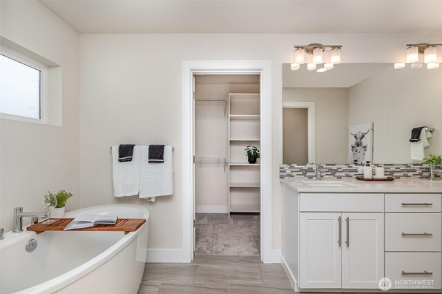 bathroom with a freestanding tub, vanity, tasteful backsplash, baseboards, and a spacious closet