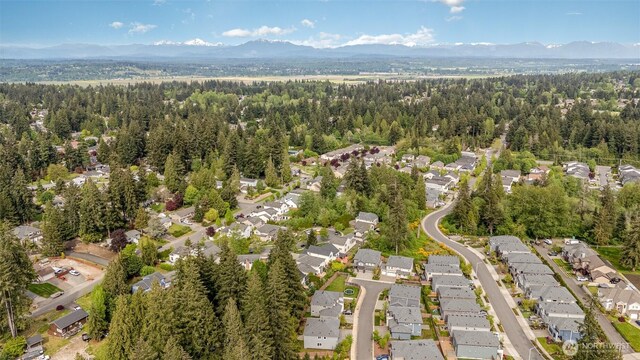 aerial overview of property's location with a mountain backdrop, nearby suburban area, and a forest