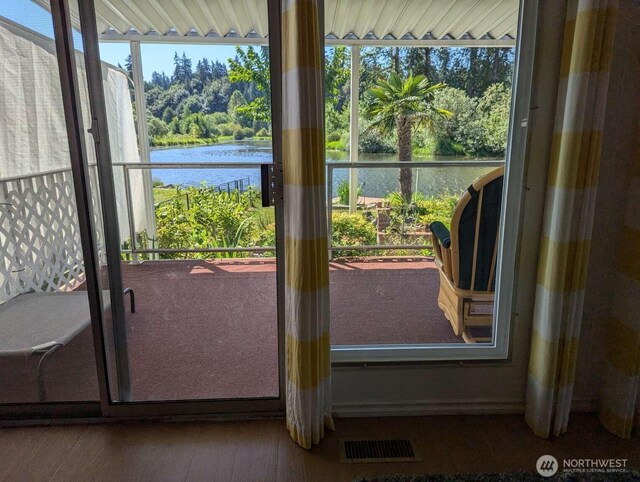 doorway with a water view, wood finished floors, and view of wooded area