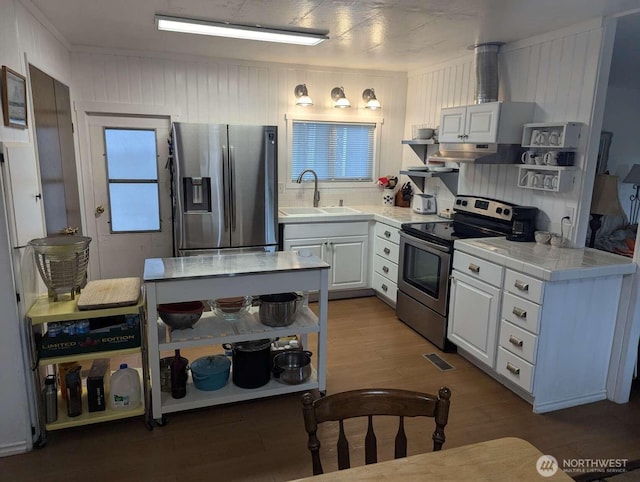 kitchen with appliances with stainless steel finishes, a sink, tile counters, wood finished floors, and white cabinets