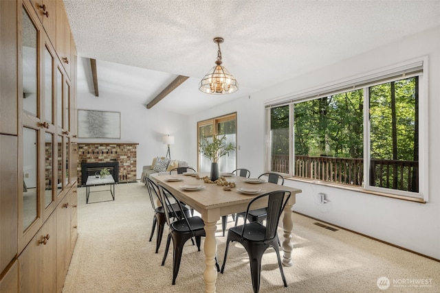 dining area featuring light carpet, a chandelier, beam ceiling, a brick fireplace, and a textured ceiling
