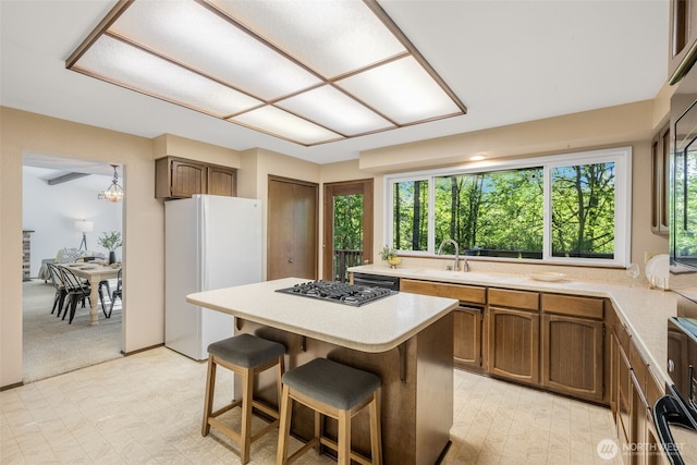 kitchen with freestanding refrigerator, a sink, stainless steel gas stovetop, light countertops, and a kitchen island