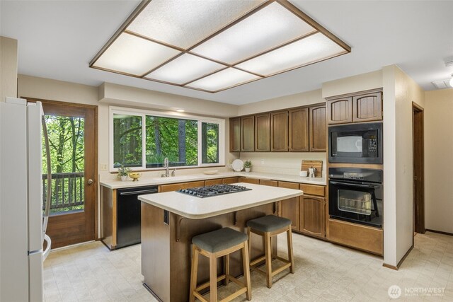 kitchen with black appliances, a sink, light countertops, a center island, and plenty of natural light