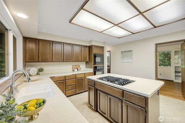 kitchen with black appliances, a sink, light countertops, light floors, and a center island
