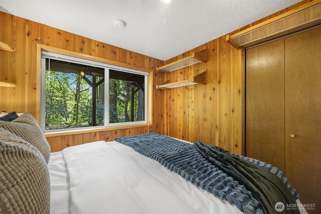 bedroom with wooden walls, a textured ceiling, and a closet
