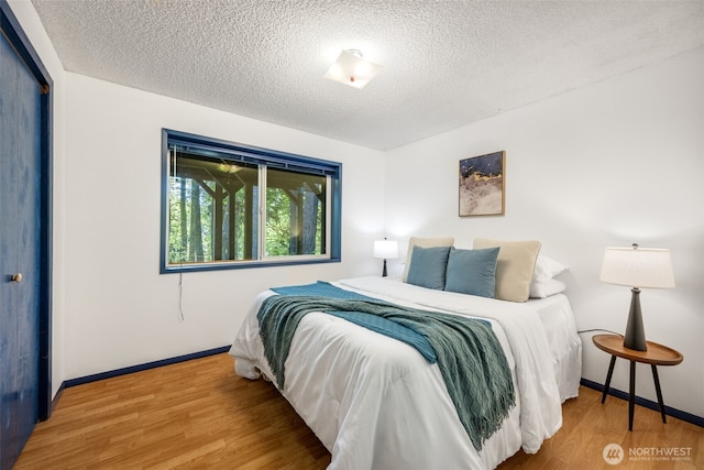 bedroom featuring a textured ceiling, baseboards, and wood finished floors
