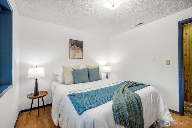 bedroom featuring wood finished floors, a textured ceiling, and baseboards