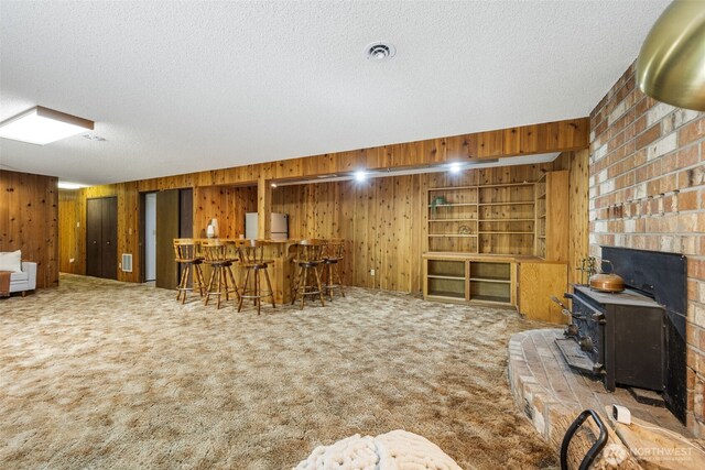 living area featuring wooden walls, bar area, a wood stove, carpet floors, and a textured ceiling