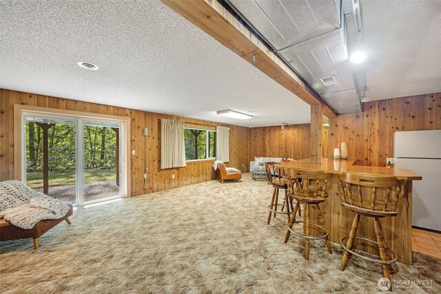 indoor dry bar featuring freestanding refrigerator, wooden walls, carpet, and a textured ceiling