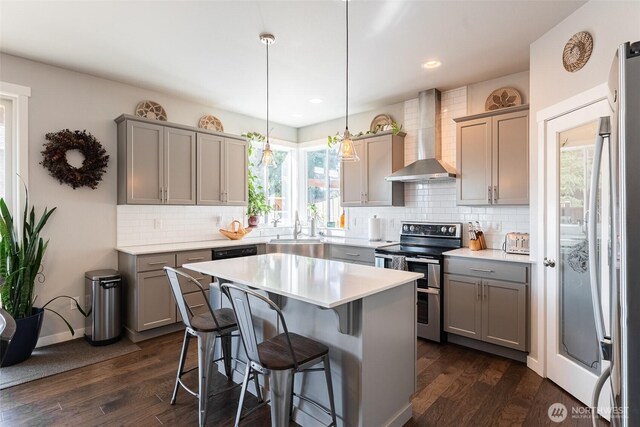 kitchen with appliances with stainless steel finishes, wall chimney range hood, gray cabinets, a sink, and recessed lighting