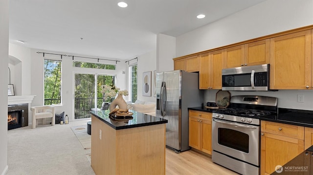kitchen with stainless steel appliances, dark countertops, a kitchen island, a premium fireplace, and recessed lighting