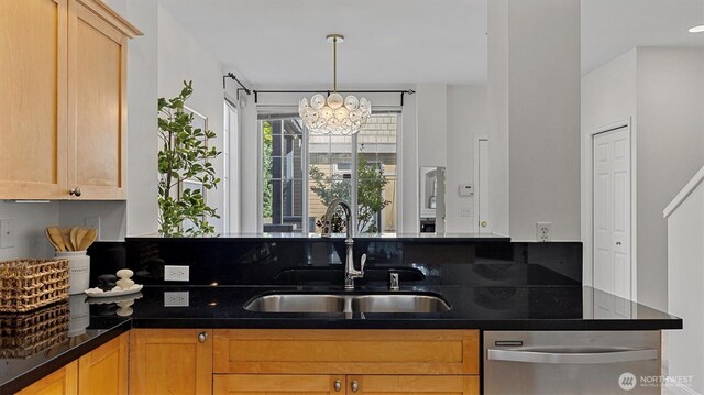 kitchen with dishwasher, a sink, dark countertops, and a chandelier
