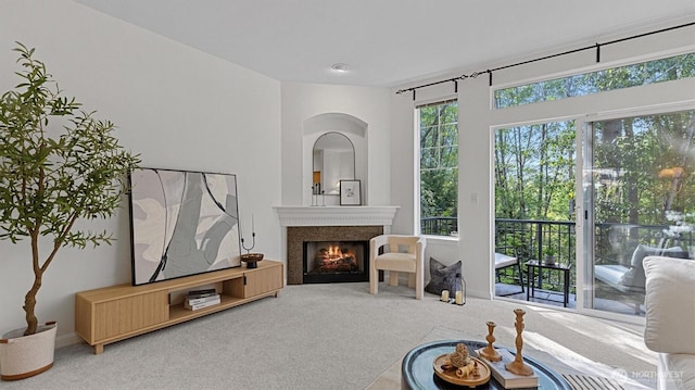 carpeted living area featuring a warm lit fireplace