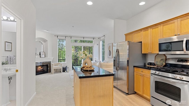 kitchen with appliances with stainless steel finishes, a kitchen island, dark countertops, a premium fireplace, and recessed lighting