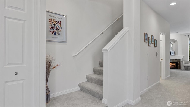 stairway featuring carpet, baseboards, a lit fireplace, and recessed lighting