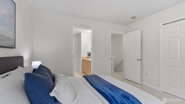 bedroom featuring baseboards, light colored carpet, and ensuite bathroom