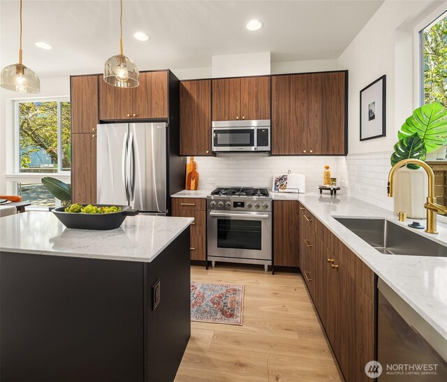 kitchen with appliances with stainless steel finishes, a sink, light wood-style floors, backsplash, and decorative light fixtures