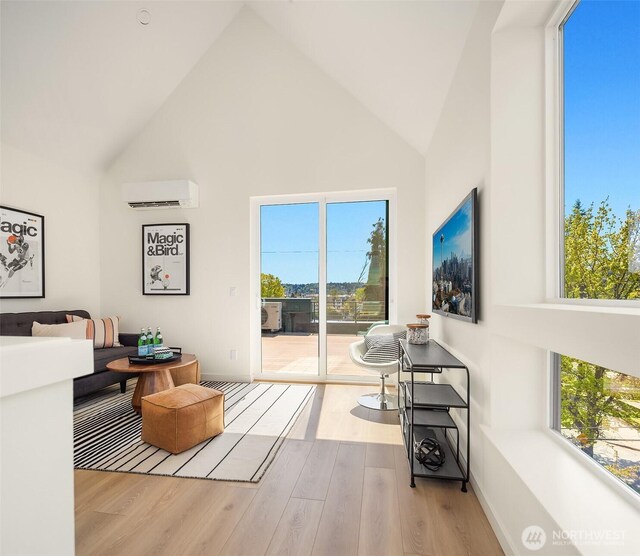 living room featuring high vaulted ceiling, an AC wall unit, wood finished floors, healthy amount of natural light, and baseboards