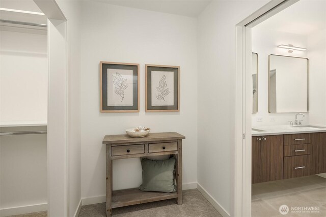corridor with a sink, light carpet, and baseboards