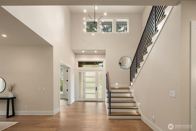 entryway with a chandelier, stairs, healthy amount of natural light, wood finished floors, and a towering ceiling