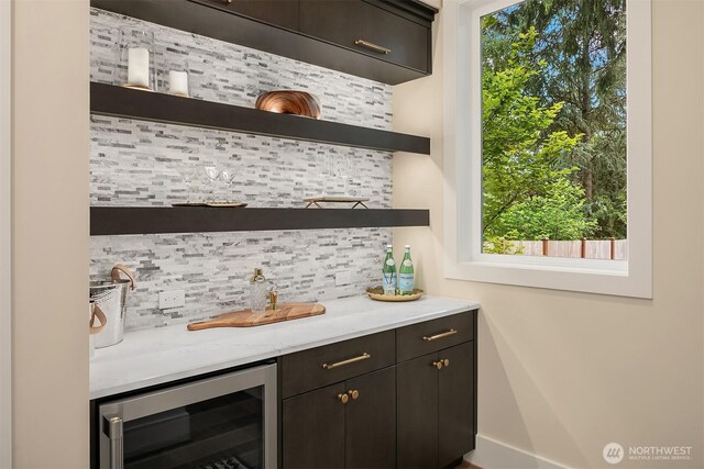 indoor wet bar featuring wine cooler, decorative backsplash, and baseboards
