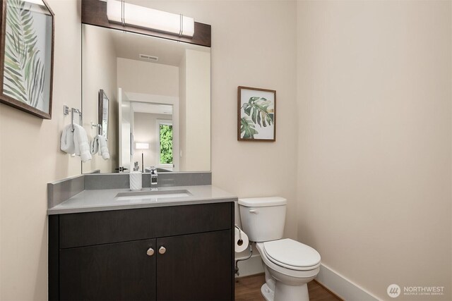 half bathroom featuring toilet, vanity, baseboards, and wood finished floors
