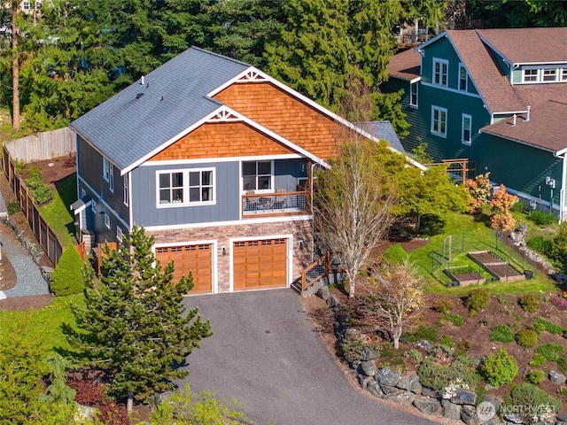 view of front of home with stone siding, an attached garage, asphalt driveway, and fence