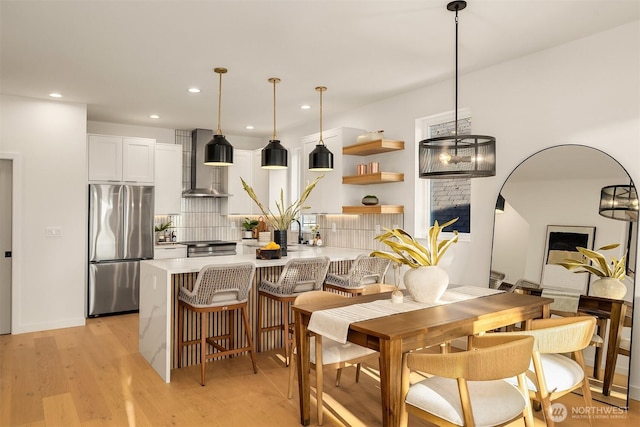 kitchen with stainless steel fridge, wall chimney exhaust hood, decorative backsplash, white cabinets, and recessed lighting