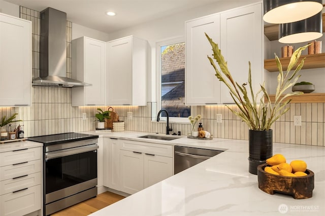 kitchen with stainless steel appliances, wall chimney exhaust hood, a sink, backsplash, and white cabinetry