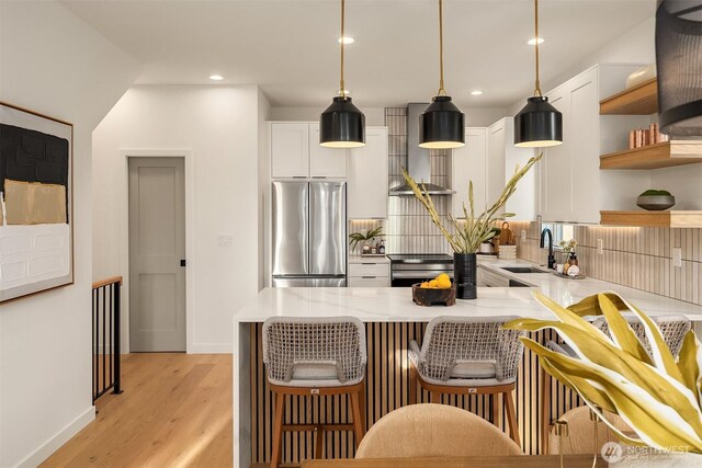kitchen with appliances with stainless steel finishes, a sink, wall chimney range hood, open shelves, and white cabinets