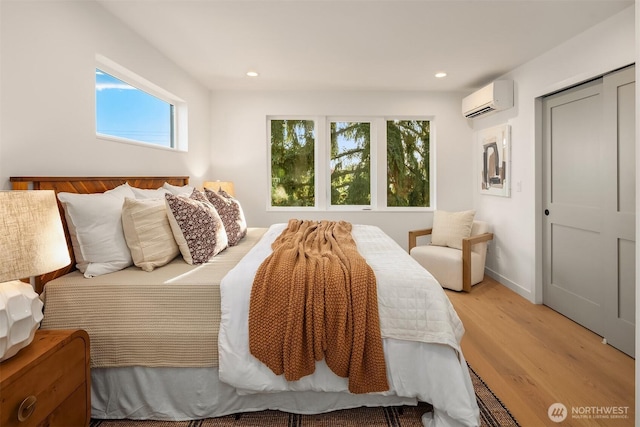 bedroom with multiple windows, an AC wall unit, light wood finished floors, and recessed lighting