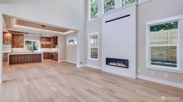 1593 213th Ct NE, Sammamish, WA 98074 - unfurnished living room with light wood-type flooring, a large fireplace, a tray ceiling, and a chandelier