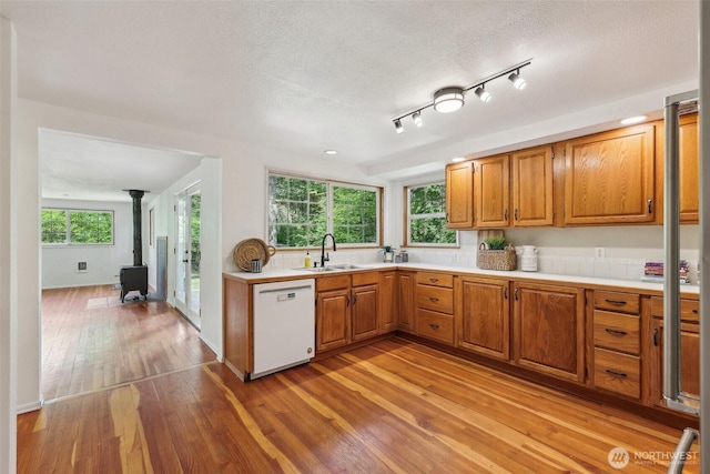 kitchen with white dishwasher, a sink, a wood stove, light wood-style flooring, and light countertops