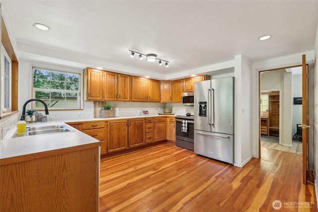 kitchen featuring stainless steel appliances, a sink, light wood-style flooring, light countertops, and brown cabinetry