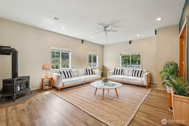 living room featuring ceiling fan, wood finished floors, recessed lighting, baseboards, and a wood stove
